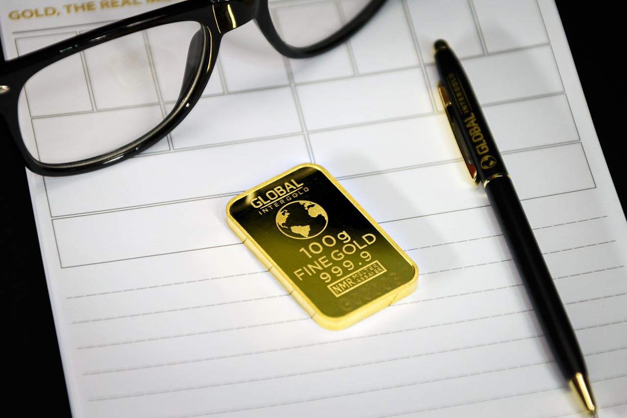 Gold bullion on notepad with eyeglasses and pen, symbolizing wealth and business planning.